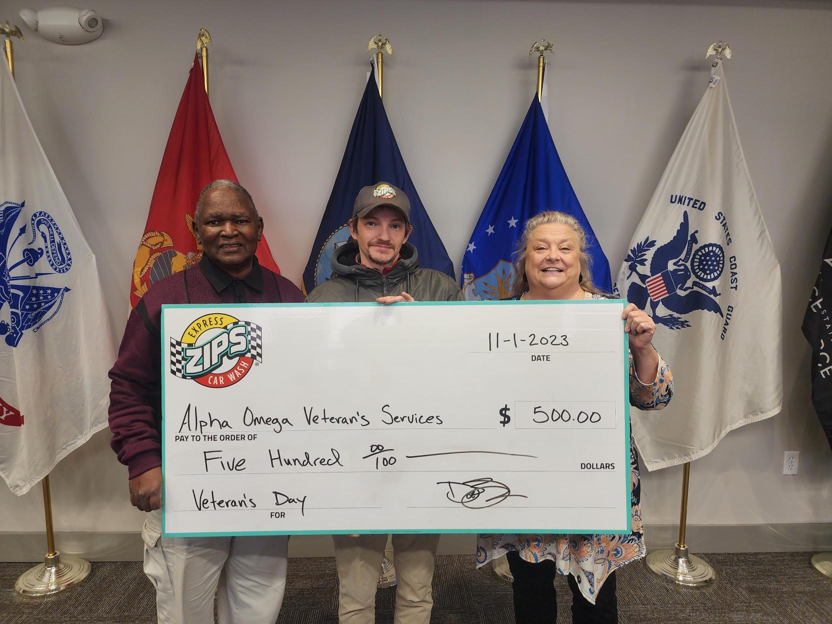 A group of three representatives from Alpha Omega Veterans Services hold a large check for $500 from ZIPS Car Wash for Veteran's Day