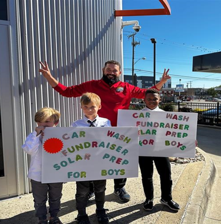 An adult and three children hold up signs advertising a ZIPS car wash fundraiser for Solar Preparatory School outside their local ZIPS Car Wash
