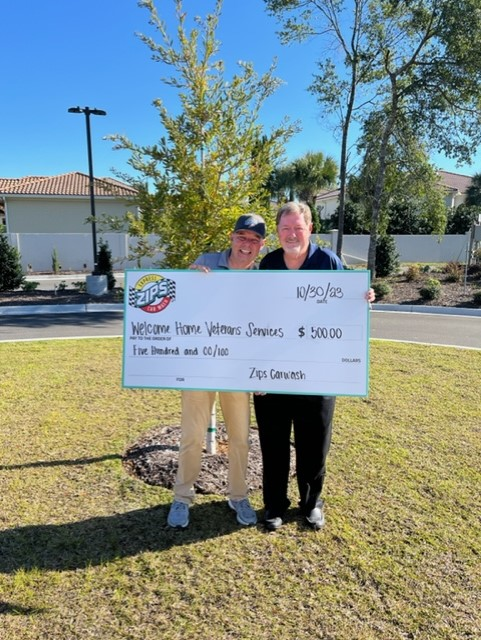 Two adults representing Welcome Home Veterans Services hold a large check for $500 from ZIPS Car Wash